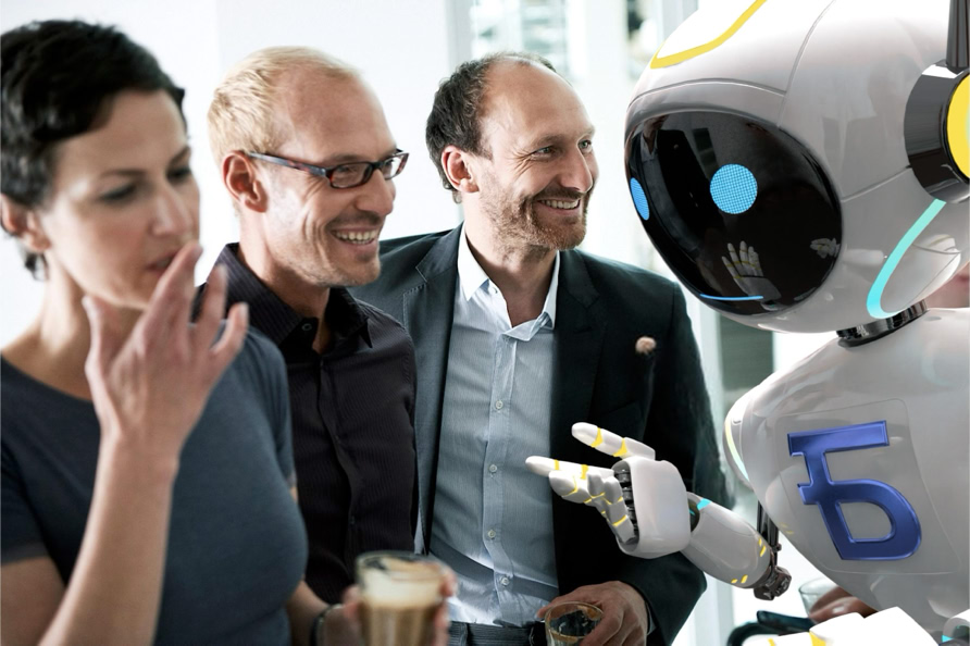 A group of three people interacting with a humanoid robot, with one person holding a drink.